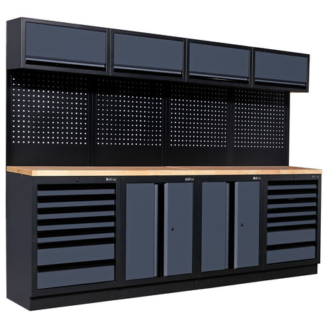 A modular workshop workbench from Bullram Werkstatteinrichtung, featuring a solid wooden worktop, dark grey cabinets and drawers for storage, a black perforated pegboard, and four matching overhead cabinets. This type of workshop furniture is available on toprools.com.